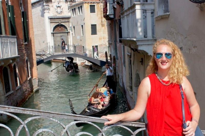 Picture of a lady smiling and posing at the bridge over a canal in Venice, Italy.