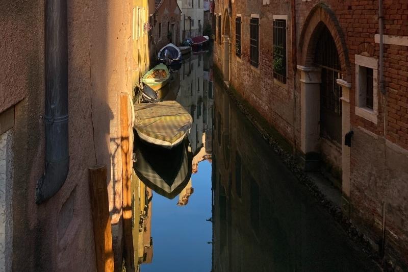 Image of an archway in the wall near a canal with gondolas lining the canal.