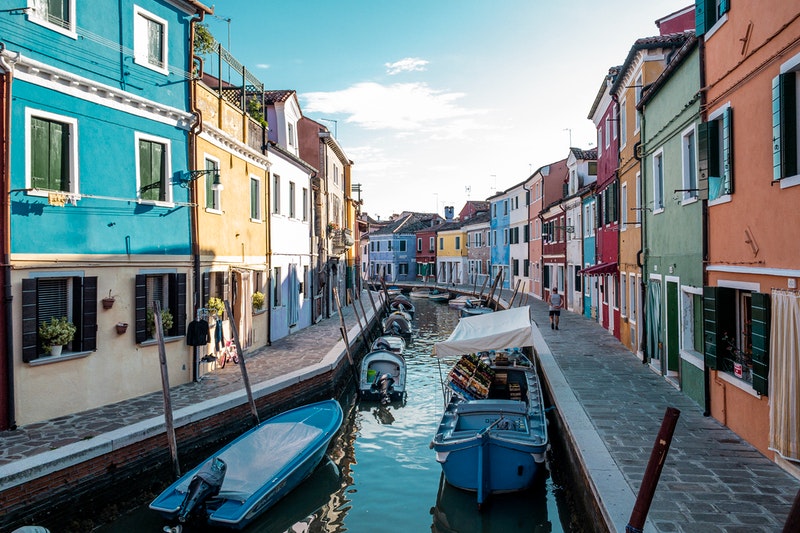 Image of colorful buildings lining the canals in Burano, Italy. Gondolas are in the canals too.